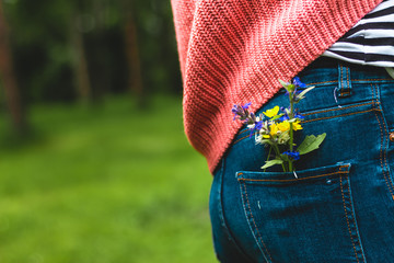 Rear view of a young woman wearing a pink crochet blouse and a pair of jeans with a small wild...