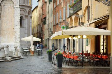 Beautifully decorated small outdoor restaurant tables in the city of Lucca, Italy - obrazy, fototapety, plakaty
