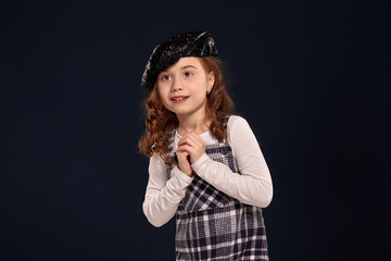 Stylish brunette kid is posing in studio on a black background. Children's fashion.