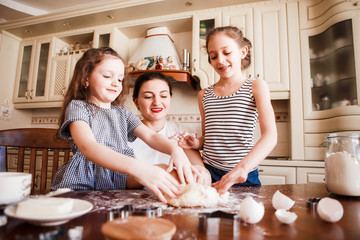 Fototapeta premium Mom and daughters prepare pastries in the bright classic kitchen. Creative mess on the table. Life style.