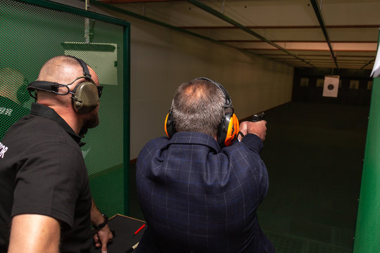Shooting in the dash of short-barreled weapons. A man aims at a target before firing a pistol. The instructor in special ballistic headphones controls the process