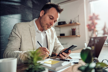 Businessman holding smart phone and writing on a adhesive notes