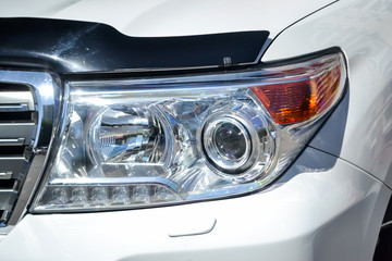 Front headlight view of car in white color after cleaning and detailing with washer before sale. Big lamp on vehicle with led drl.