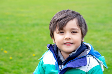Head shot of happy kid sitting in the park with bright light sunny day, Portrait child playing outdoor in spring with blurry green grass park background, Positive children concept