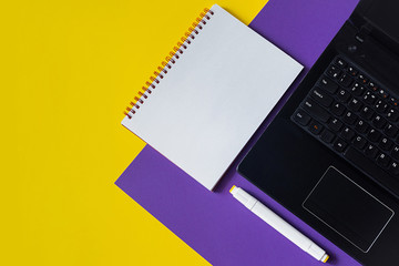 Office table with blank notebook and laptop. Mockup on yellow and purple minimalist geometric background