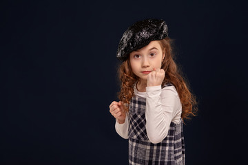 Stylish brunette kid is posing in studio on a black background. Children's fashion.