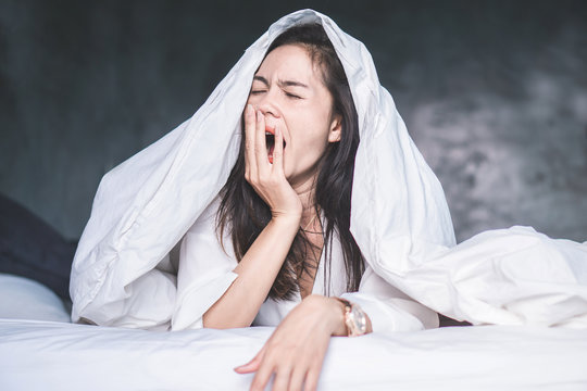 sleepless Asian woman wake up on bed and yawning feeling tired 
