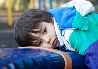 Protrait lonely child lying down and looking in side way in playground,Sad boy playing alone at the park,Poor kid with thinking face looking out waiting for some one at play area