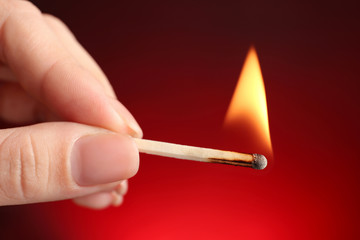 Woman holding burning match on color background, closeup