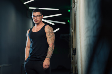 Young strong man in gym in glasses and tanktop