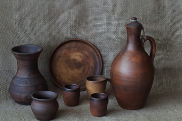 Set of earthenware crockery: jug for wine, round dish, glasses, vase, pot, mug on homemade jute...