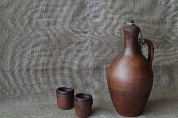 Pottery, wine set: clay jar and cups on a rough jute homespun cloth. Concept — kitchen utensils,...
