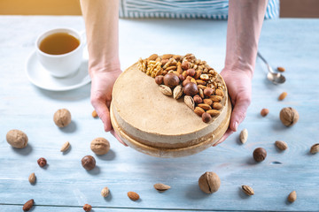 Raw nutty cake decorated with walnut, almond, hazelnut on a blue background. Gluten free food. Vegan dessert.