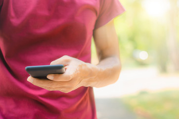 close up handsome man use left hand typing mobile phones and touch screen working with app devices in park with sunrise and green blur nature background.