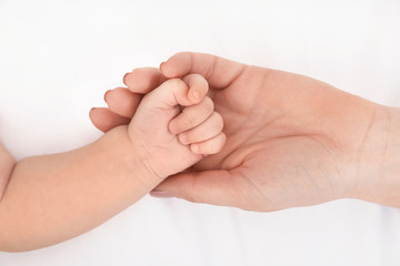 Mother holding her baby's hand on bed, top view
