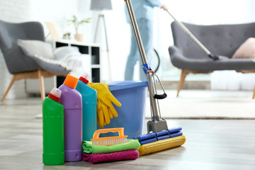 Detergents, bucket and mop on floor with janitor vacuuming carpet indoors