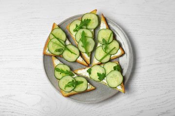 Plate with traditional English cucumber sandwiches on white wooden background, top view