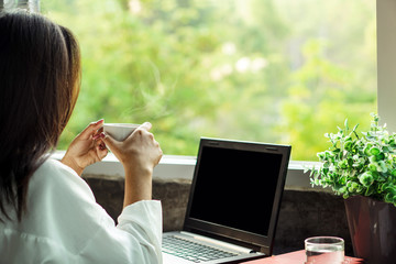 Asian business woman drinking coffee at home office enjoying the view of nature from window with...