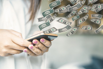 woman hand holding smart phone transfer money online with paper currency flying 