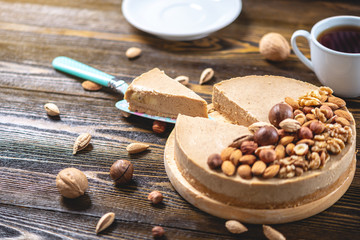 Nutty caramel cheesecake cake with topping of walnut, almond, hazelnut and macadamia on a dark wooden background.