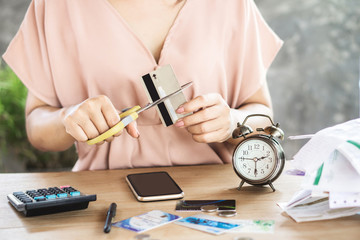 Asian business woman hand cutting credit card by scissors with mobile phone, calculator and bills on desk