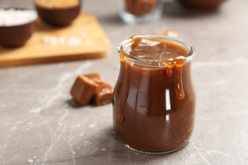 Jar with tasty caramel sauce on grey table. Space for text