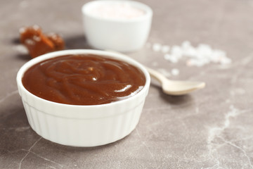 Bowl with tasty caramel sauce on grey table. Space for text