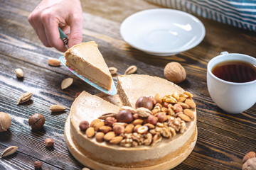 Nutty caramel cheesecake cake with topping of walnut, almond, hazelnut and macadamia on a dark wooden background.