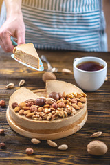 Nutty cheesecake on a dark wooden background. Confectioner in a blue apron holding a piece of nut cake
