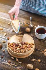 Nutty cheesecake on a dark wooden background. Confectioner in a blue apron holding a piece of nut cake