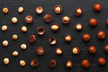 Fototapeta na wymiar Purified and shell repeats macadamia nuts on black textural stone background. Healthy eating concept