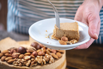 Nutty cheesecake on a dark wooden background. Confectioner in a blue apron holding a piece of nut cake
