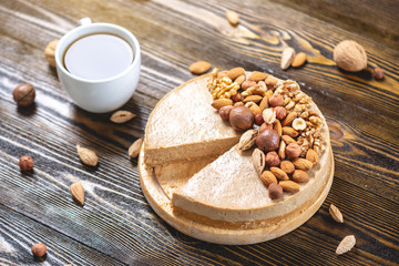 Nutty caramel cheesecake cake with topping of walnut, almond, hazelnut and macadamia on a dark wooden background.