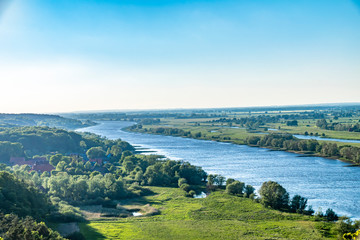 View over the Elbauen in Lower Saxony, Germany. You see a landscape with fields, meadows and the river Elbe under a blue sky.