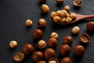 Shelled macadamia nut and peeled macadamia nut on a black textural background in a wooden spoon