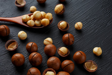 Shelled macadamia nut and peeled macadamia nut on a black textural background in a wooden spoon