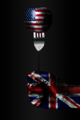 A hand with a drawn Great Britain flag holds a fork, on which is a ball with a drawn USA flag, a...