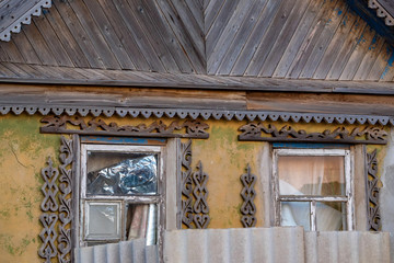 Close up facade of old rural house. View of broken windows with wooden decoration