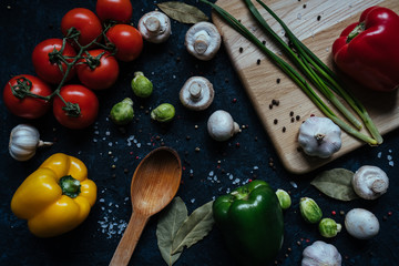 Fresh, organic vegetables on black stone background. Ripe tomatoes, cucumbers, broccoli, green onion and garlic and wooden board. Healthy vegetarian food. Top view. Flat lay