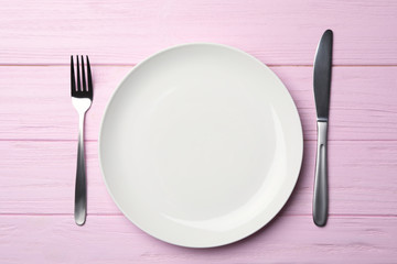 Stylish ceramic plate and cutlery on wooden background, flat lay