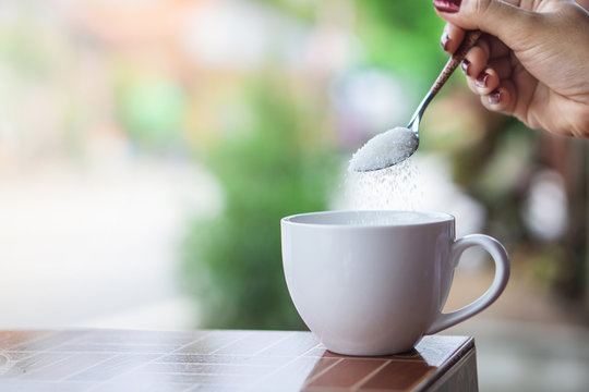 unhealthy woman hand holding spoon pouring sugar in to coffee cup