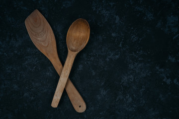Wooden spatula and a spoon for frying on pans isolated on black table background. Top view. Copy space. Kitchenware, cooking utensils. Your text