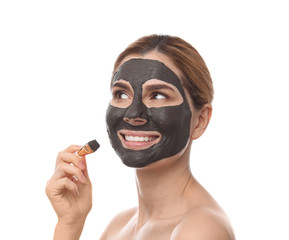 Beautiful woman applying black mask onto face against white background