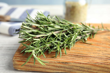 Wooden board with fresh rosemary twigs on table