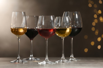 Glasses with different wines on grey table against defocused lights