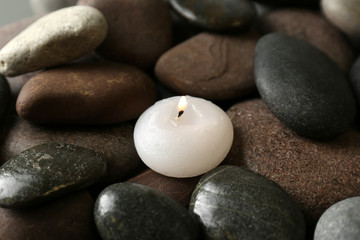 Fototapeta na wymiar Small burning candle on beautiful spa stones