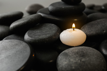 Fototapeta na wymiar Small burning candle on beautiful spa stones, space for text