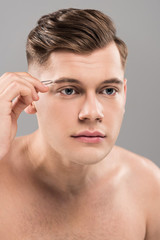 focused young man using eyebrow tweezers isolated on grey