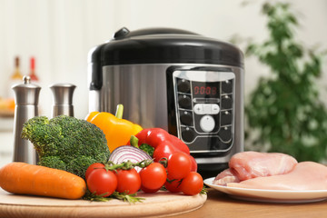 Modern multi cooker and ingredients on wooden table in kitchen