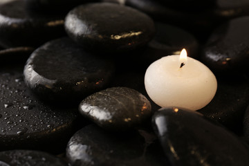 Fototapeta na wymiar Small burning candle on beautiful wet spa stones, space for text
